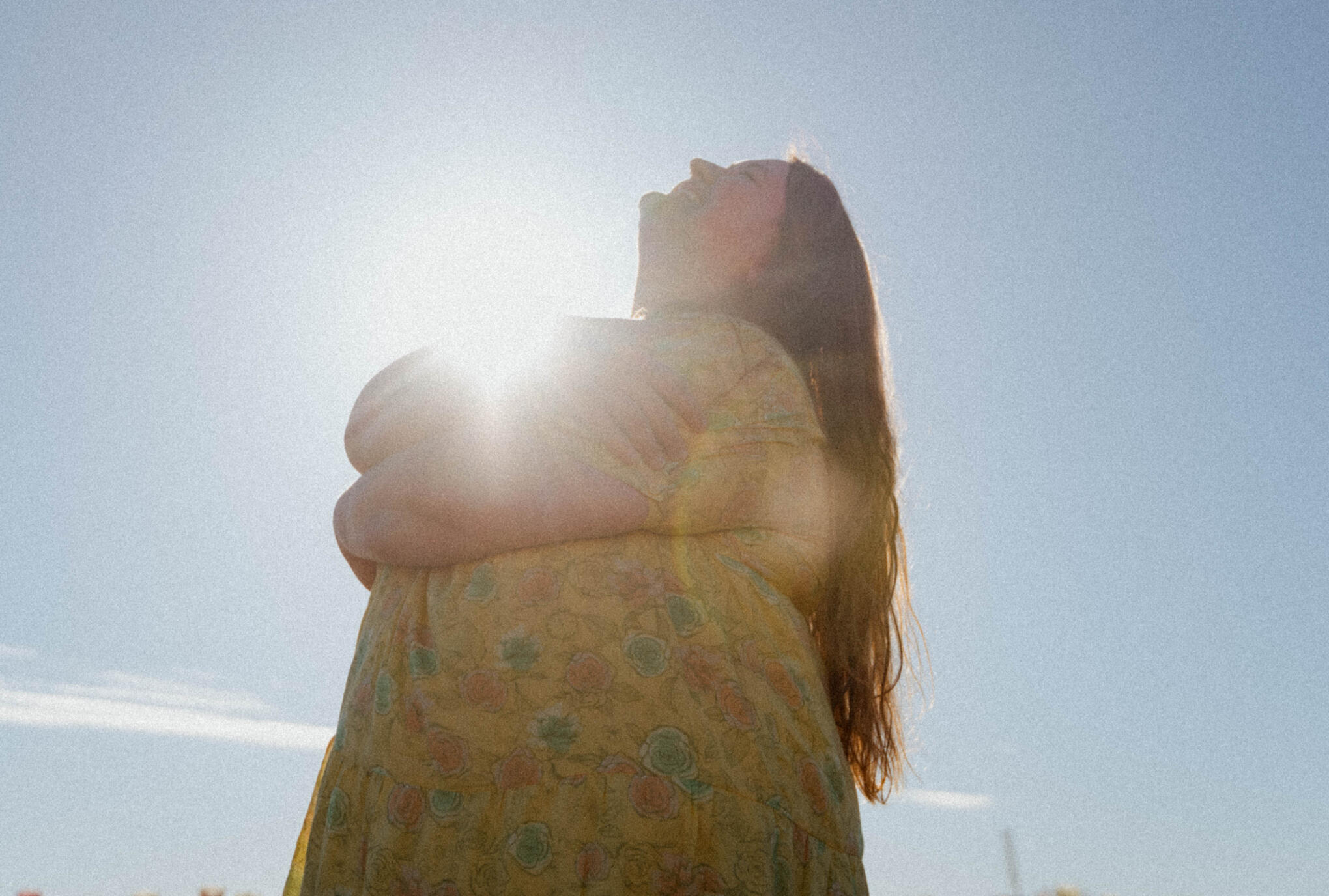 a fat woman embraces herself on a sunny day. She smiles upward toward the sky.