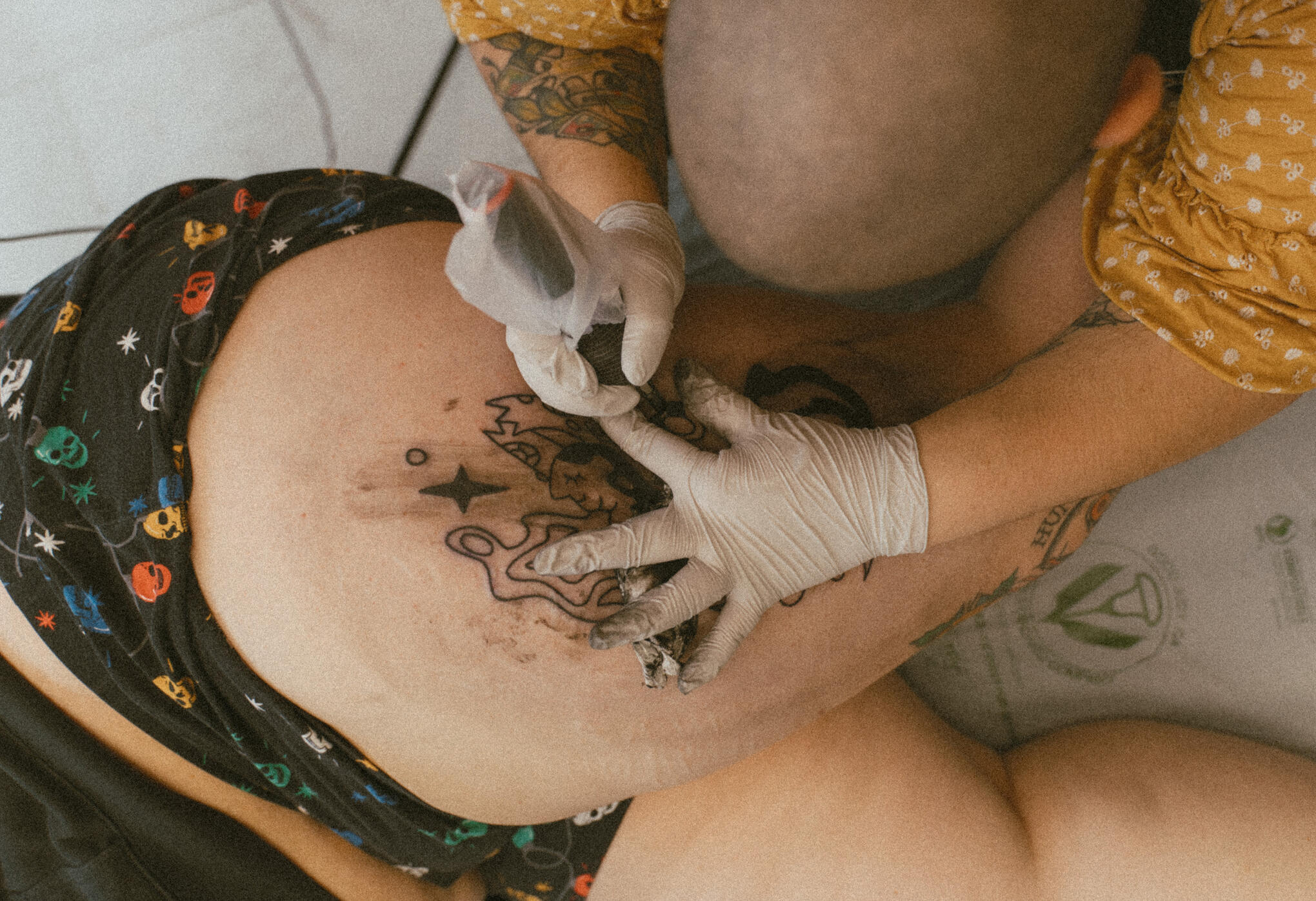 A close up photo of a tattoo artist working on a thigh tattoo. Both the artist and the client are fat individuals.